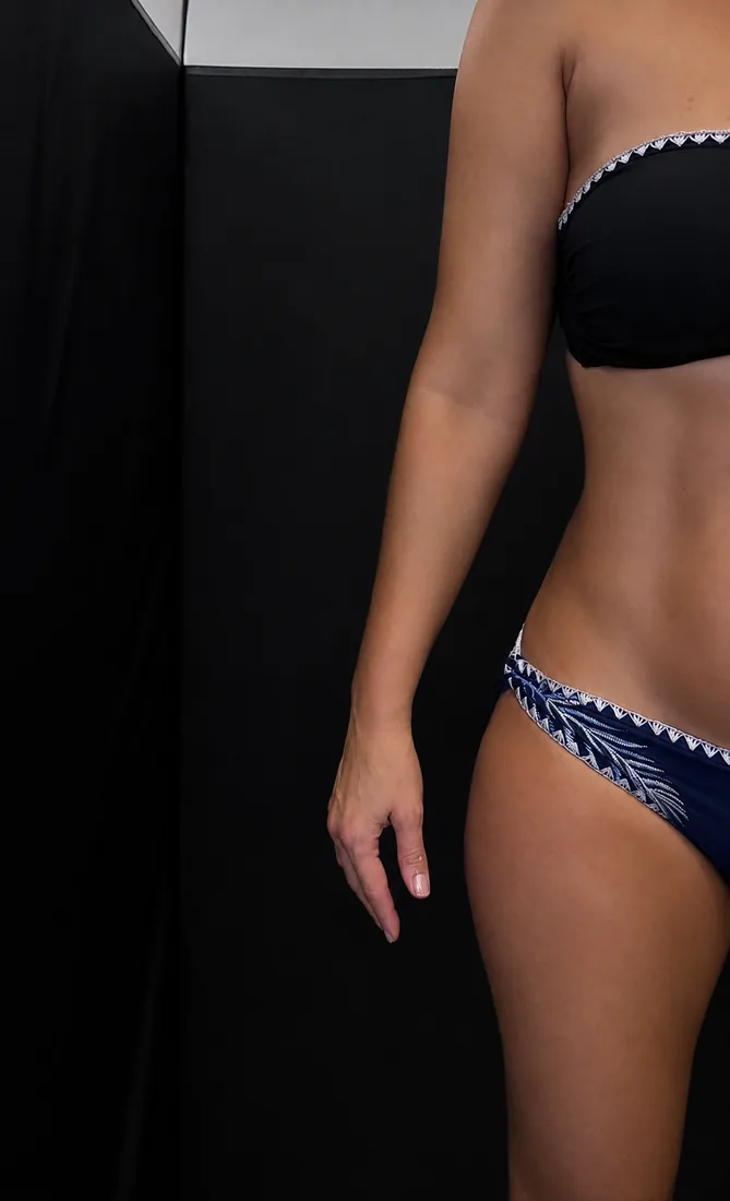 Spray tan result in a navy bikini against a black backdrop