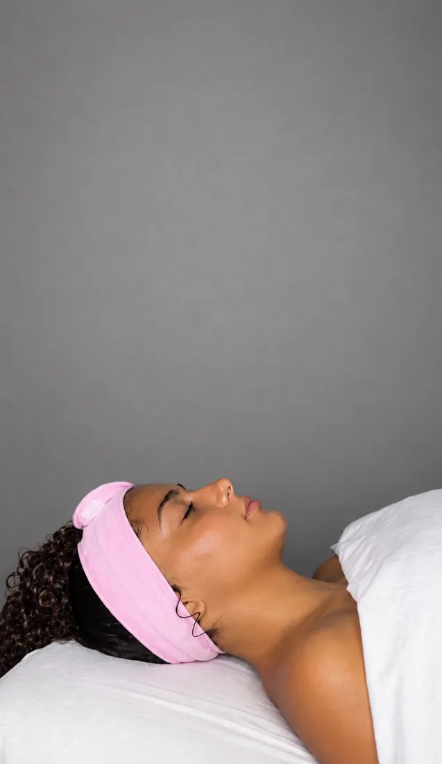 Client resting during a facial, eyes closed, wearing a pink headband